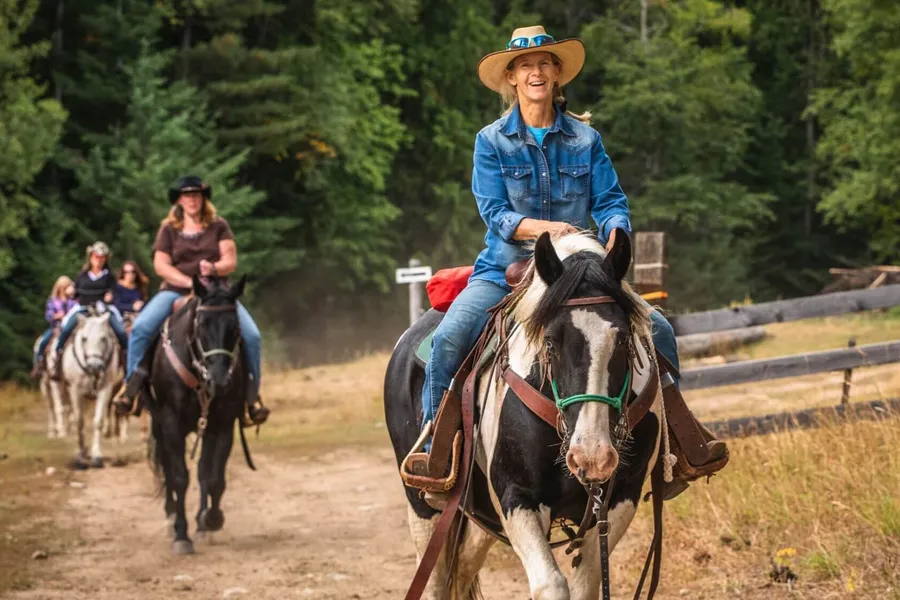 woman on gypsy vanner horse riding with other people on horseback behind her