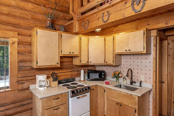 Wrangler Cabin kitchen, with a stove, sink and coffee maker, and horseshoes on the beam below the loft