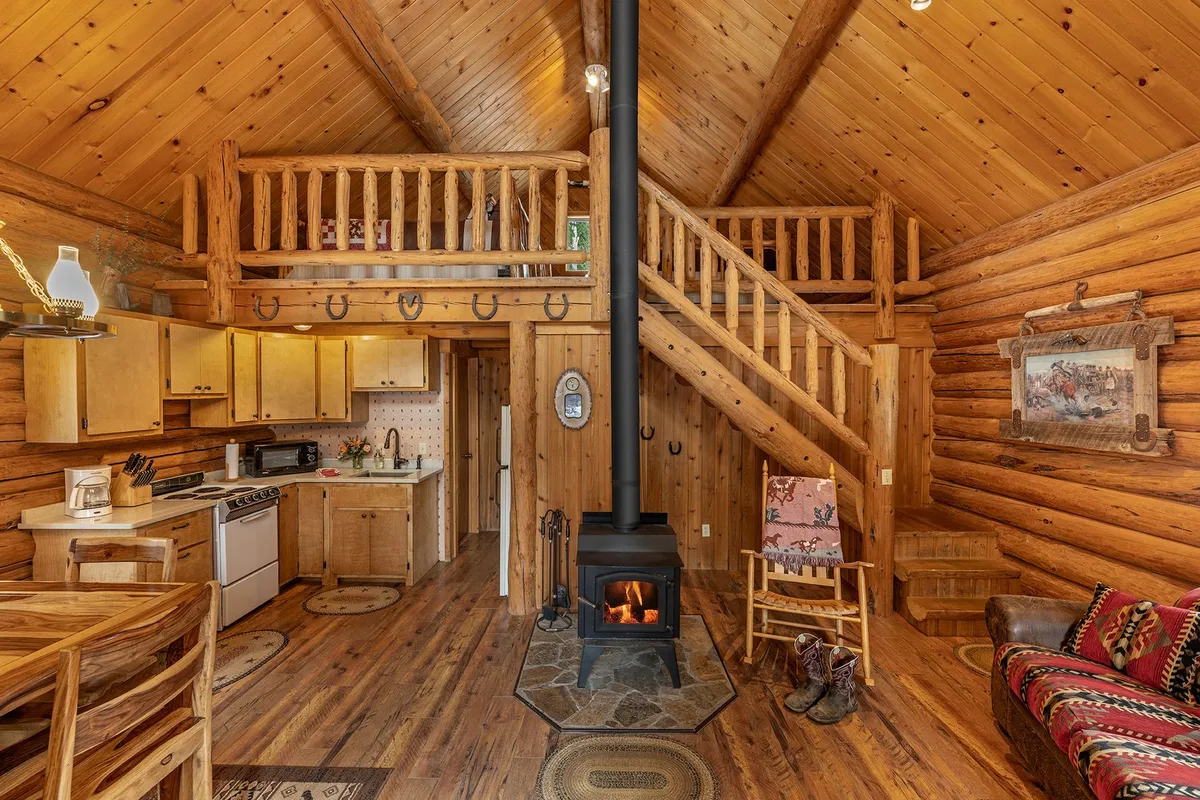 Main room of the Wrangler Cabin, with a wood stove burning, a rocking chair, the kitchen, and log stairs up to the loft