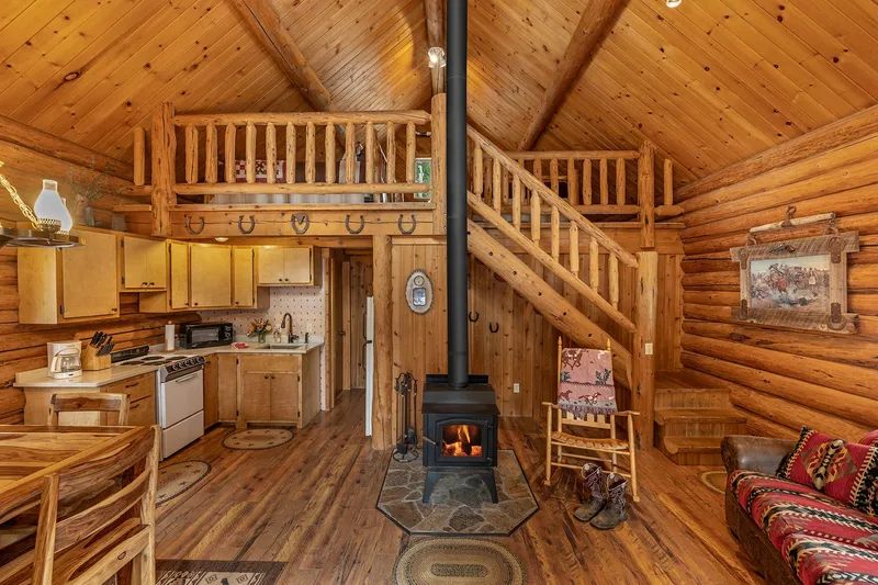 Main room of the Wrangler Cabin, with a wood stove burning, a rocking chair, the kitchen, and log stairs up to the loft