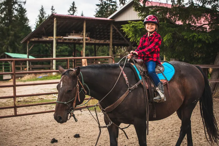 Grinning young rider in a helmet sitting on a dark bay horse beside the pole barn