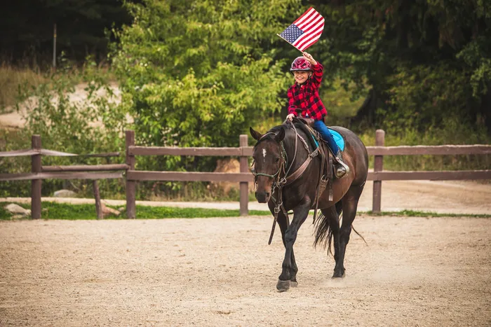Young rider waving an American flag while riding a dark bay horse around the arena