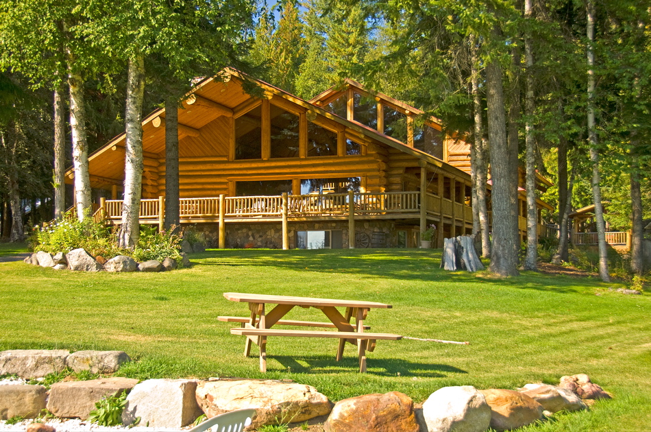 Large log lodge with green lawn and a picnic table