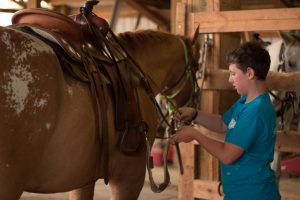 Youth Horsemanship Program with boy saddling his horse